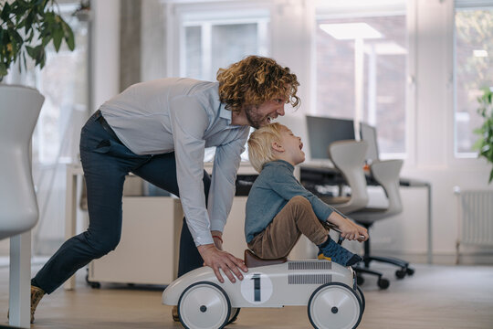 Businessman pushing son on toy car in office
