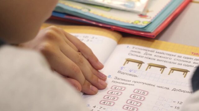 A student completing math exercises in a workbook with a pen at a desk, representing academic development, concentration, and the primary school learning process in a study setting
