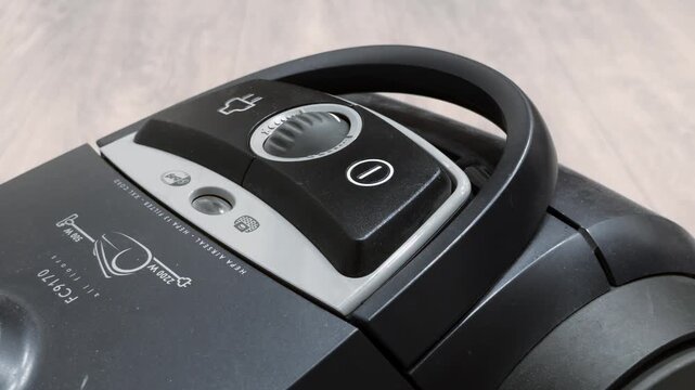 Male hand presses power button of bagged vacuum cleaner. Close up view control panel. Home cleaning equipment technology. Housework device floor care machine electronic equipment