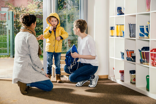 Boy in raincoat with mother and pre-school teacher in kindergarten