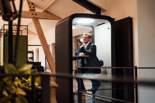 A businessman talks on a smartphone in a soundproof office booth