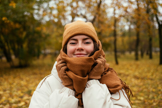 Smiling young woman wrapped up in scarf in autumn park