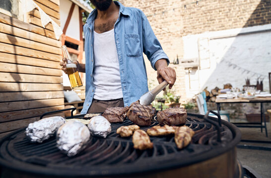 Young man preparing meat on a barbecue grill in a backyard