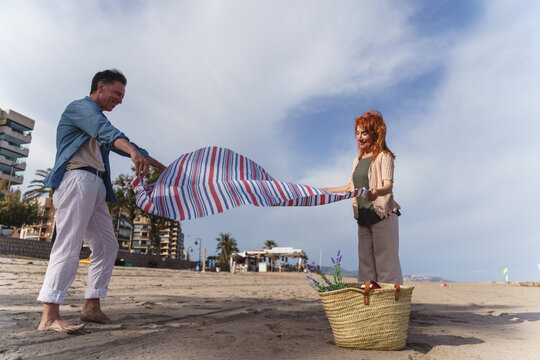 Senior couple spreads a picnic blanket on the sunny beach