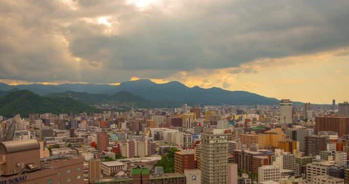 Sapporo downtown city skyline daytime timelapse with dramatic crepuscular sun rays breaking through thick clouds over mountains