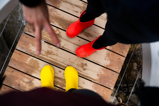 First-person view of two friends in bright waterproof boots with a peace sign gesture. Hiking, friendship and cheerful outdoor lifestyle.