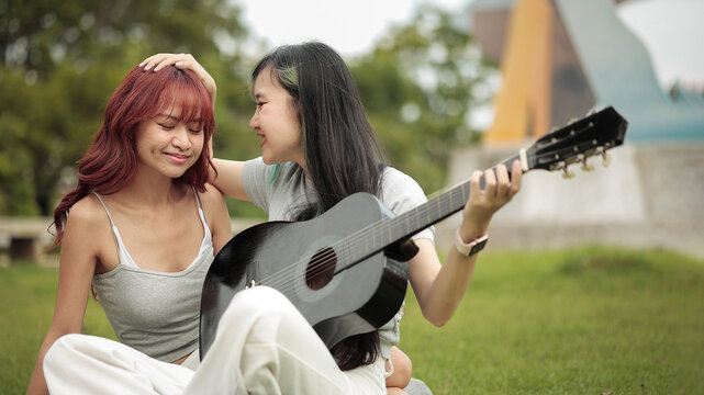 Young LGBTQ Couple Playing Acoustic Guitar in Park, Love, Music, Friendship and Inclusive Lifestyle Outdoors