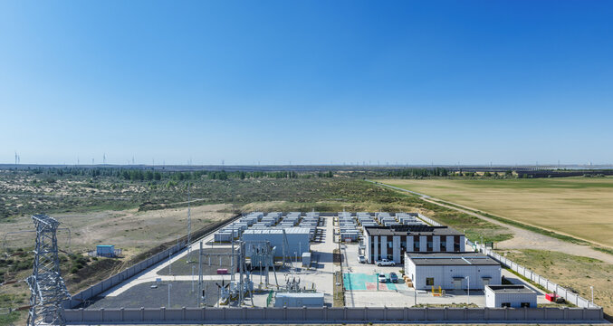 Aerial View of a Battery Energy Storage Station in Arid Grassland with Wind Turbines and Solar Arrays in Distance