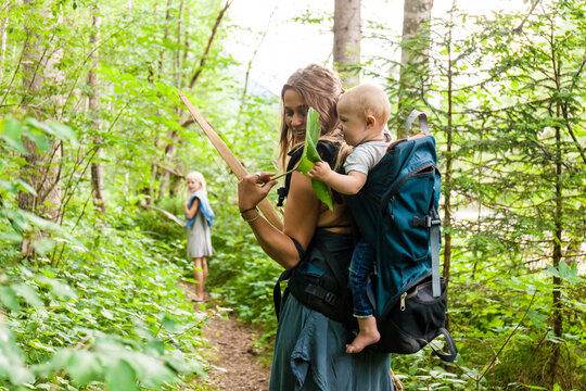 Woman hiking in the woods showing large leaf to baby boy in backpack