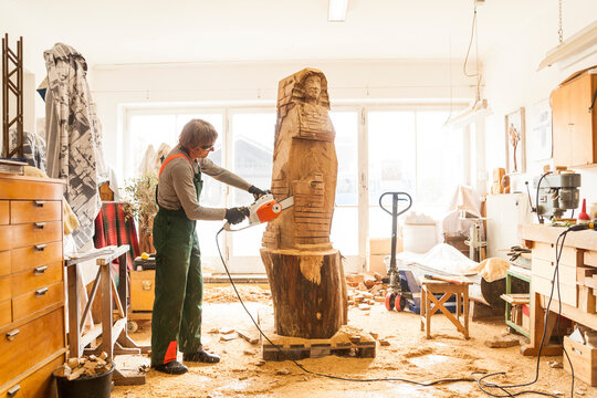 Wood carver in workshop working on sculpture with chainsaw