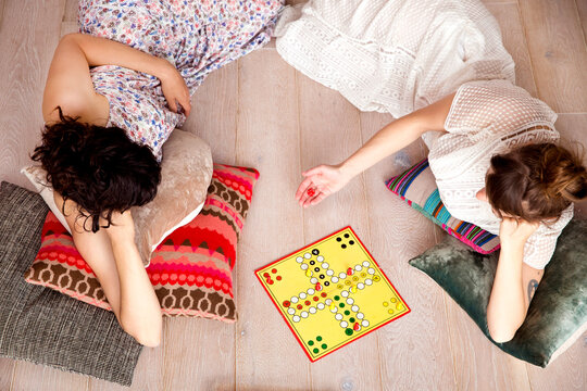 Top view of two best friends lying on the floor at home playing ludo