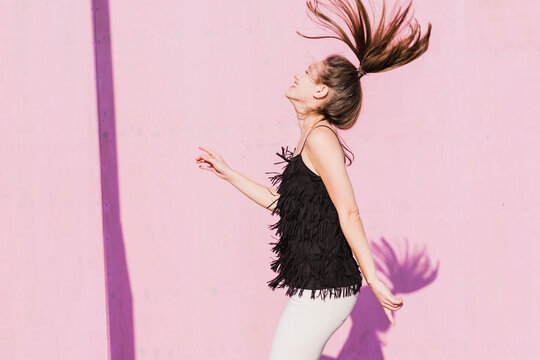 Happy young woman moving in front of pink wall