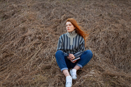 Student with red hair sitting in a field holding a notebook