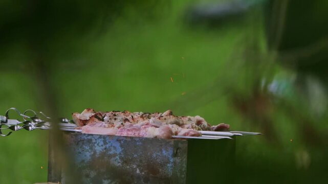 Meat skewers cooking on rustic charcoal brazier with sparks flying outdoors in summer. Juicy pork chicken pieces grilled over open flame, preparation of outdoor meal, copy space