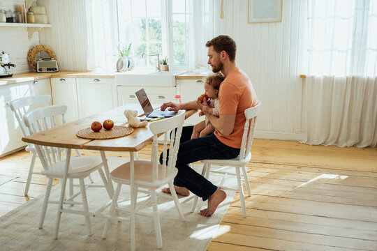 Businessman feeding daughter while working on laptop at home