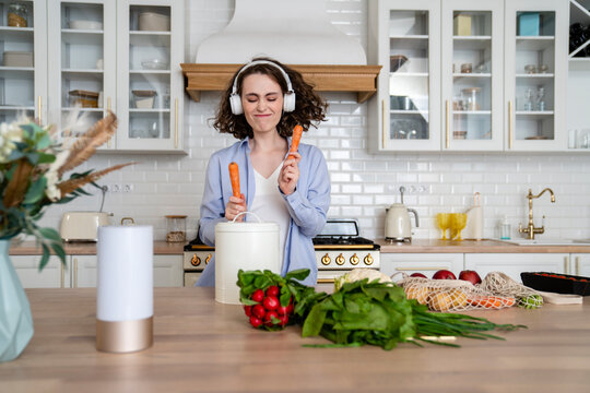 Smiling woman listening music and playing container with carrots at home