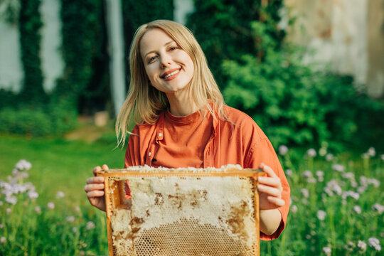 Smiling woman holds a fresh honeycomb frame in a green garden