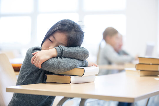 A tired schoolgirl takes a nap on a pile of books during a long day of studying at school