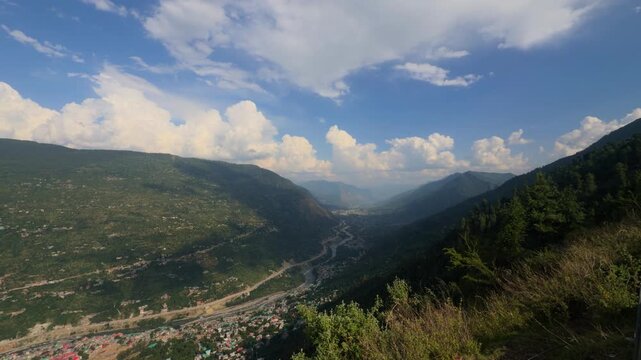 4K shot of Kullu city as seen from the nearby mountain with clouds above the Kullu valley during the monsoon season in Himachal Pradesh, India. Scenic view of Himalayan mountain city in monsoon.