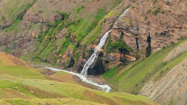 4K shot of a waterfall on side of a mountain flowing during the summer season due to melting snow in the Himalayas as seen during the Ghepan Lake Trek near Sissu in Lahaul, Himachal Pradesh, India.
