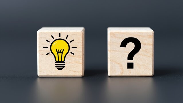 Illumination and Inquiry: Two wooden cubes, one depicting a glowing lightbulb and the other a bold question mark, are placed side-by-side, symbolizing the journey from an idea to a solution.