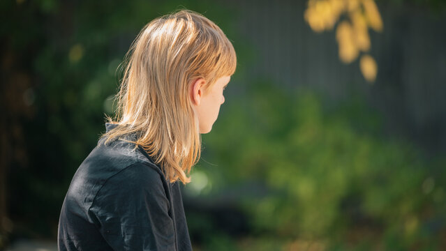 Young person with blond mullet hairstyle looking away thoughtfully in natural light