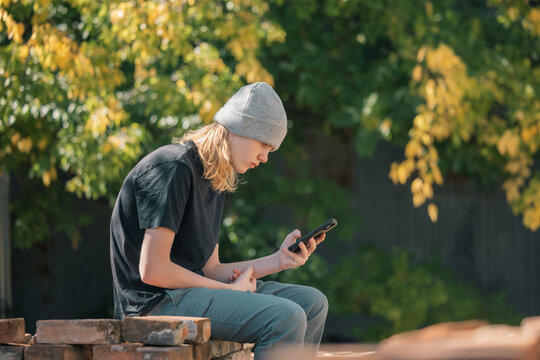 Young person in beanie using a smartphone outdoors with blurred autumn foliage background
