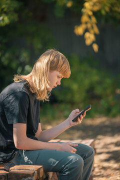 Teenage boy with blond mullet using a smartphone outdoors on a sunny day