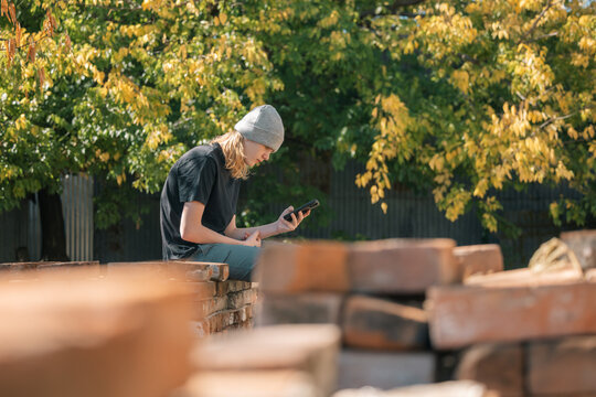 Young person wearing a beanie and looking at their phone outdoors on a sunny day