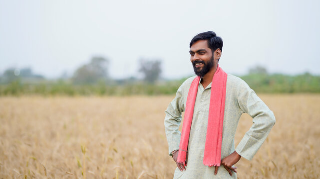 young indian farmer standing at golden wheat field