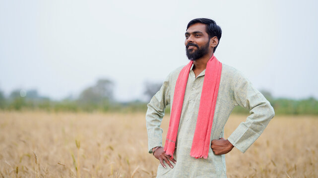 young indian farmer standing at golden wheat field