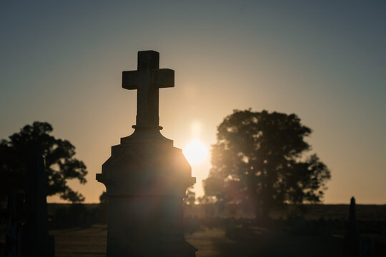 Silhouette of a cross tombstone against a golden sunrise in a cemetery
