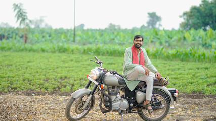 Fototapeta premium young indian farmer sitting on bike and gesturing with hand at field