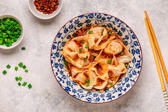 Wontons are placed in a bowl with spicy sauce.