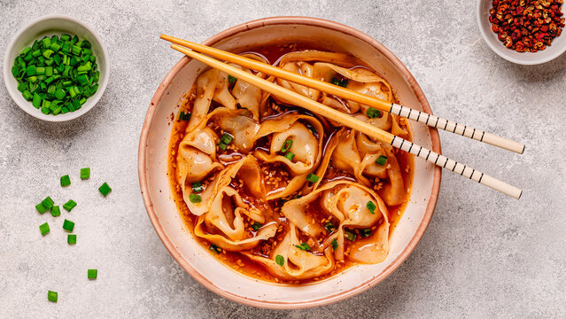 Wontons are placed in a bowl with spicy sauce.