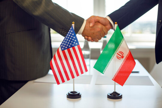 Iran USA diplomats handshake signals negotiation and agreement. Two officials in suits meet at a table with national flags, signaling treaty talks. Clear symbol of diplomacy and cooperation.