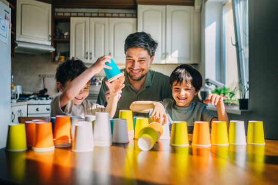 Father and sons stack colorful cups together in the kitchen