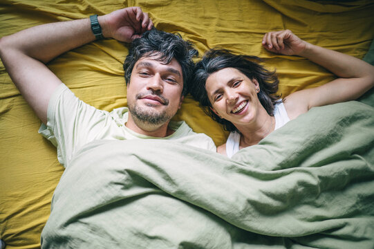 Husband and wife look at the camera from their bed