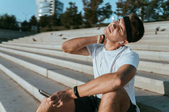 Young man stretching neck sitting on steps