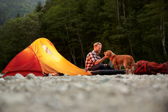 Happy businessman with dog sitting outside tent