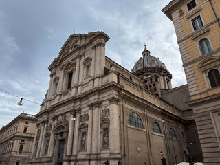 Obraz premium A classic Italian church with a stone facade and ornate dome stands in Rome, set against a soft, cloudy sky, showcasing grand European architectural heritage and historic religious artistry.