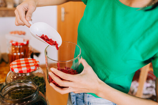 Pouring red pasta into a glass jar during zero waste bulk shopping