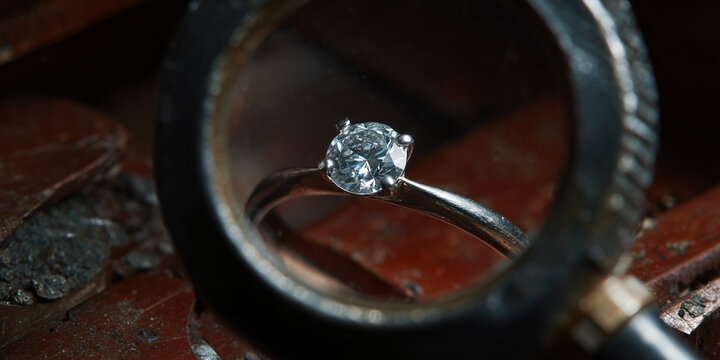 A diamond ring is viewed under a magnifying glass, highlighting its sparkle and intricate design, set against a rustic backdrop