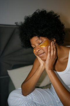 Thoughtful woman with eye patches sitting on bed in bedroom at evening