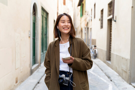 Italy, Florence, happy young woman with earphones and cell phone in an alley
