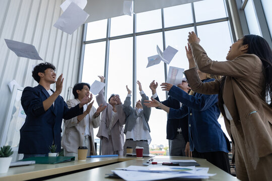 Happy business team of diverse people throwing paper in modern office celebration for huge success. Group shows incredible joy after finishing difficult project with great teamwork and victory