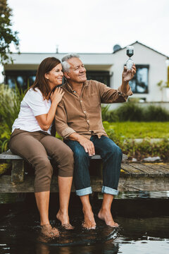Smiling couple looking at hourglass sitting on jetty by lake