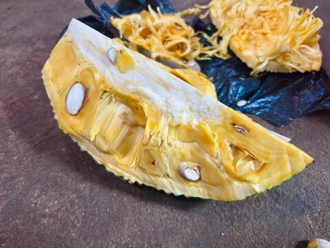 Fresh sliced jackfruit with golden yellow flesh and visible seeds on a rustic surface. Tropical fruit close-up highlighting natural texture, sweetness, healthy nutrition, and organic freshness.