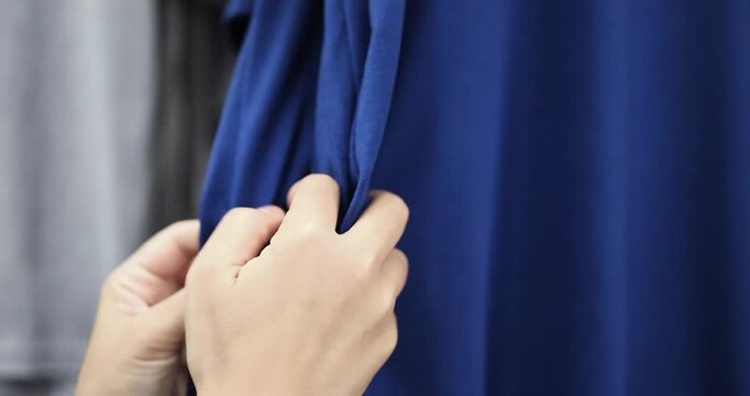 Customer browsing clothes on a clothing rack in a department store, touching and inspecting fabric while comparing garments before making a fashion purchase
