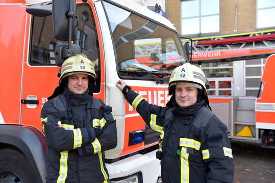 Portrait of two confident firefighters in front of fire engine